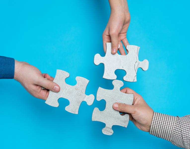 three people holding puzzle pieces, putting them together, blue background